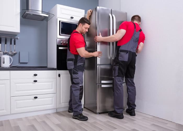 Técnicos profesionales de Solution part realizando la instalación de un refrigerador de acero inoxidable en una cocina moderna...