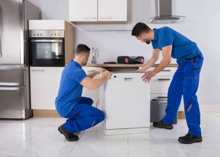 Profesionales de Solution Part en uniforme azul, ajustando y moviendo un lavavajillas para su correcta instalación
