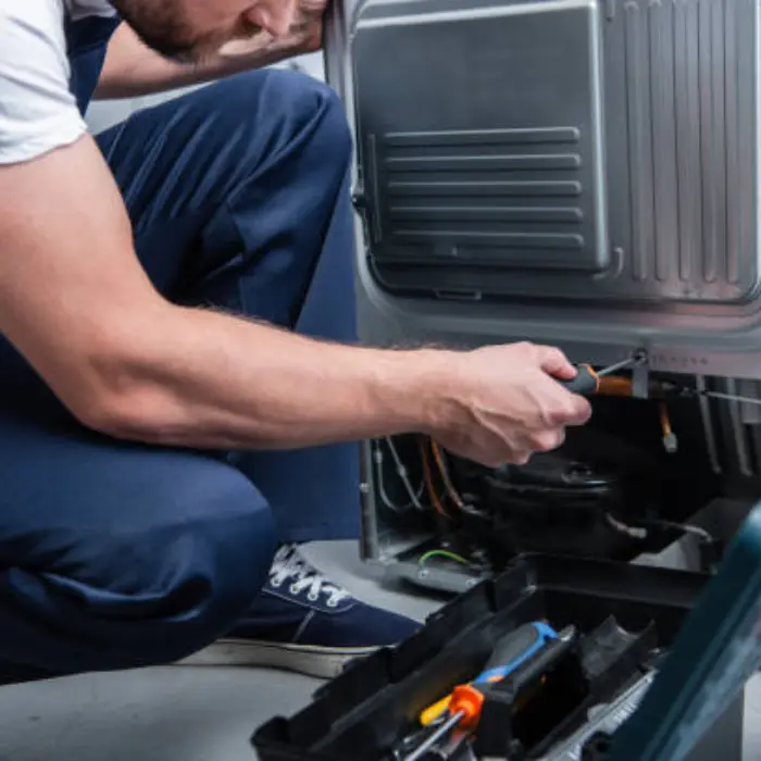 Técnico profesional de Solution Part realizando una reparación detallada en el motor de un refrigerador con su caja de herramientas en primer plano.