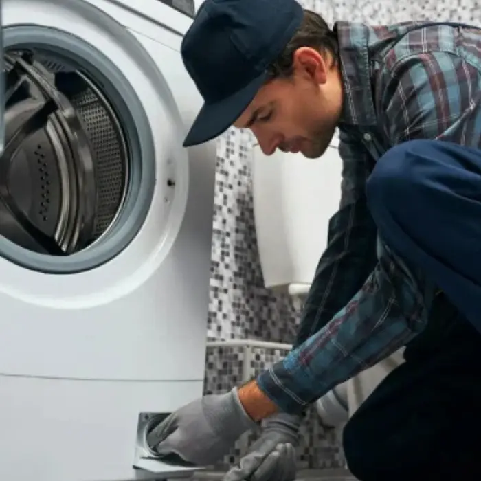 Técnico de Solution Part con guantes, arrodillado para realizar el mantenimiento del filtro de una lavadora en el domicilio del cliente.