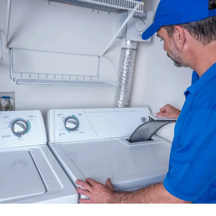 Técnico de Solution Part con uniforme azul, revisando y limpiando el filtro de pelusas de una secadora de ropa durante una visita de mantenimiento.